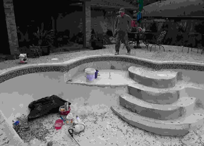 A man is standing next to a swimming pool with stairs.