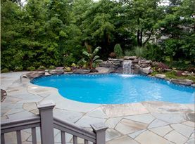 A large swimming pool with a waterfall in the backyard.