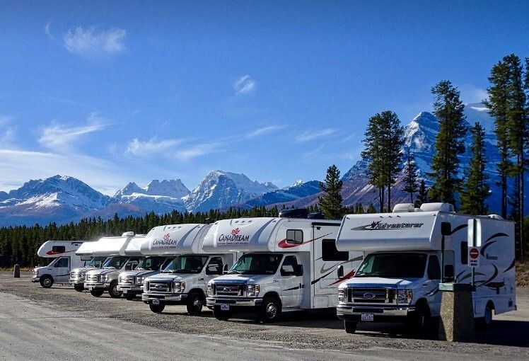 A row of rvs parked in a parking lot with mountains in the background