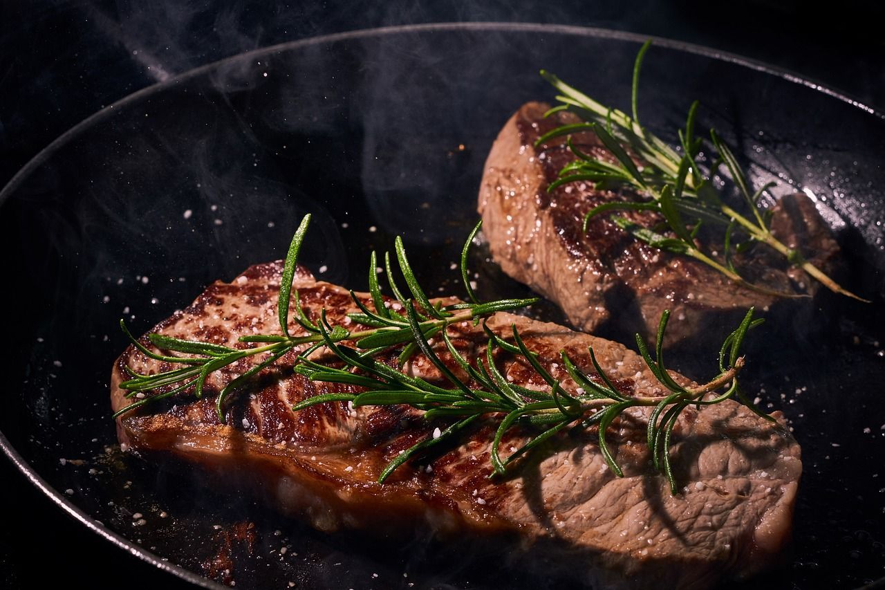 Two steaks are being cooked in a frying pan with rosemary.