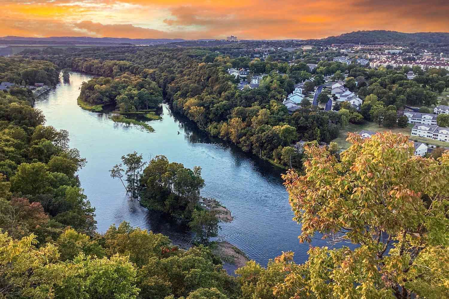 An aerial view of a river surrounded by trees and a city at sunset.