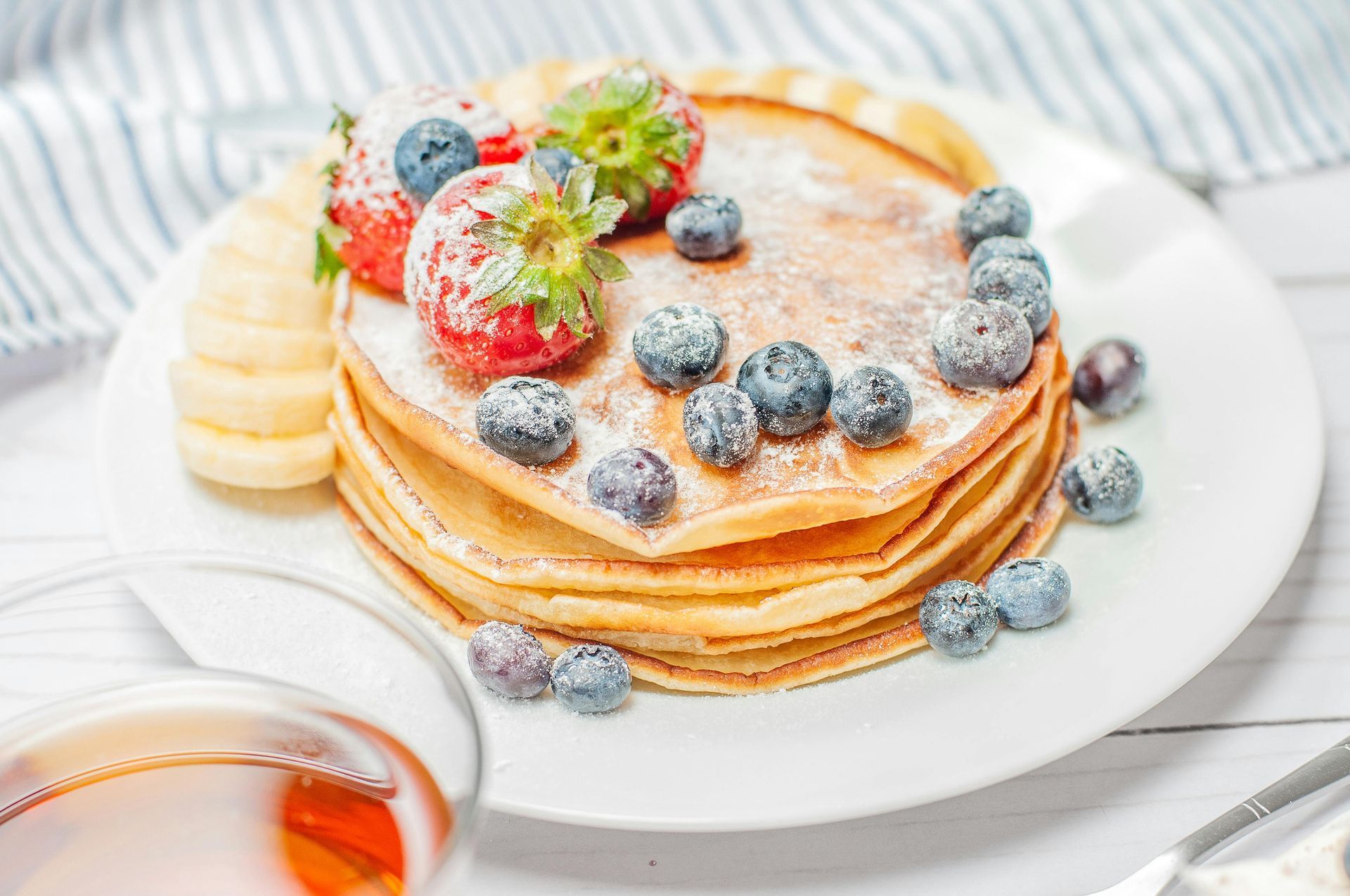 A stack of pancakes with blueberries , strawberries and bananas on a white plate.