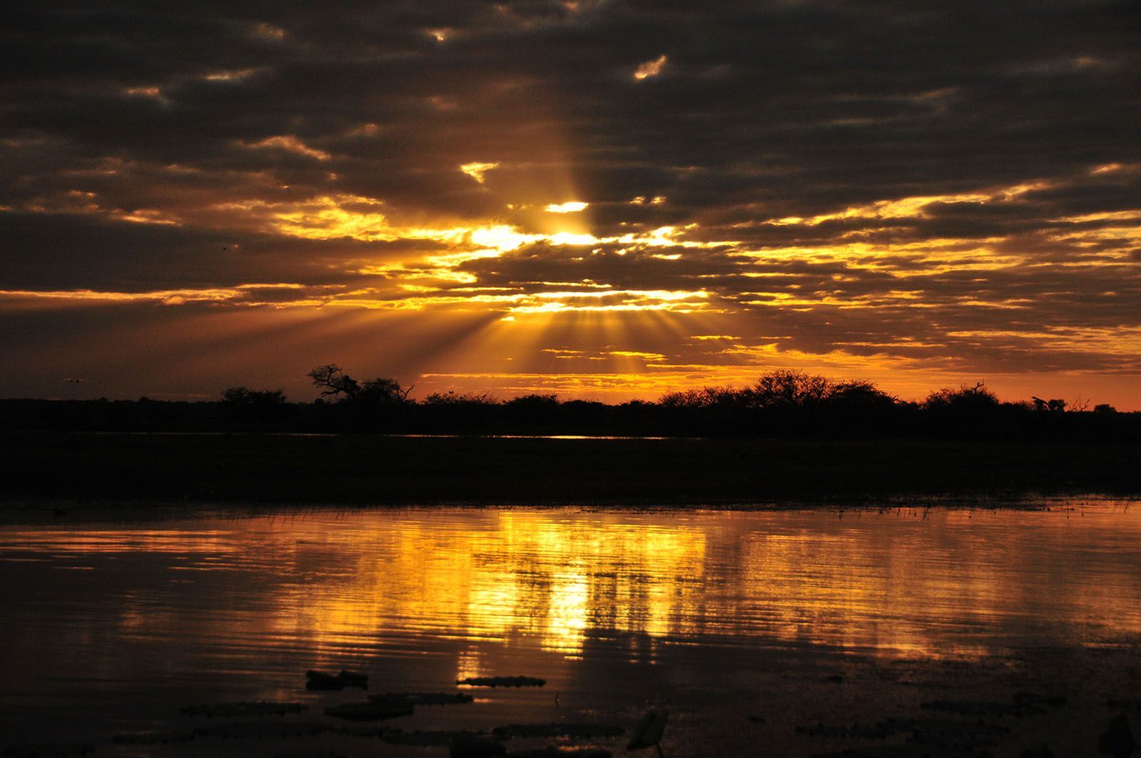 A sunset over a body of water with the sun shining through the clouds