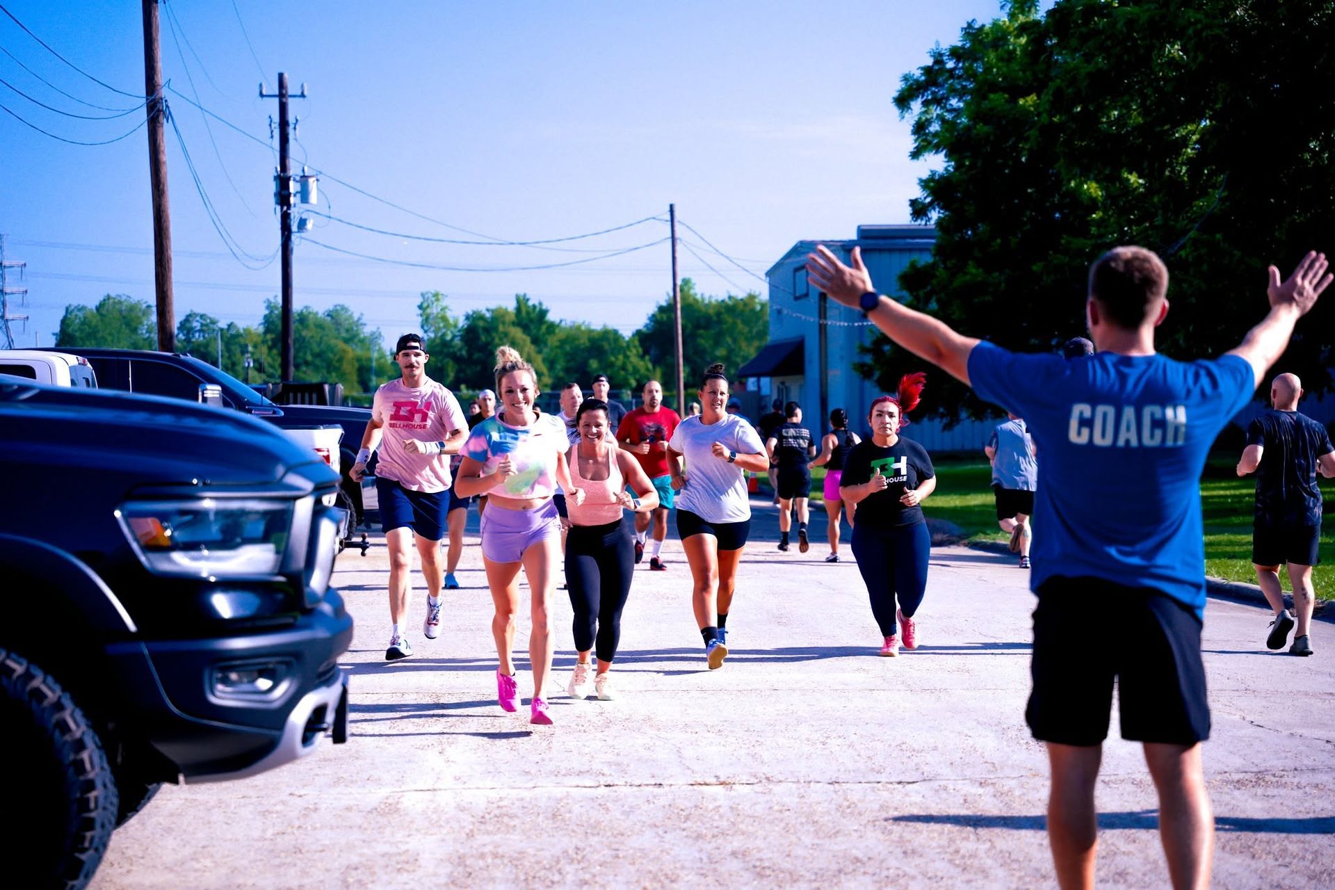 Runners approaching a finish line as a race official in a blue shirt raises both arms on a sunny street