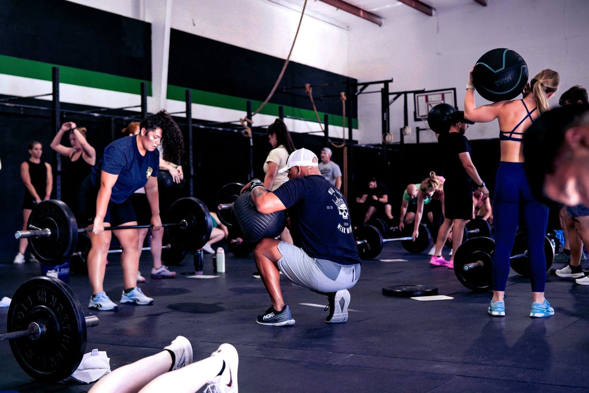 People doing CrossFit-style exercises in a gym, with dumbbells and barbells on the floor.