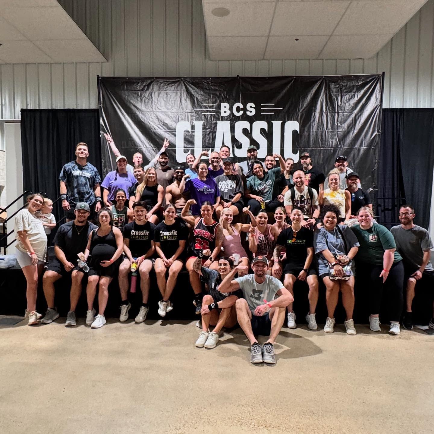 Large group posing in front of a black “BCS Classic” banner at an indoor event.