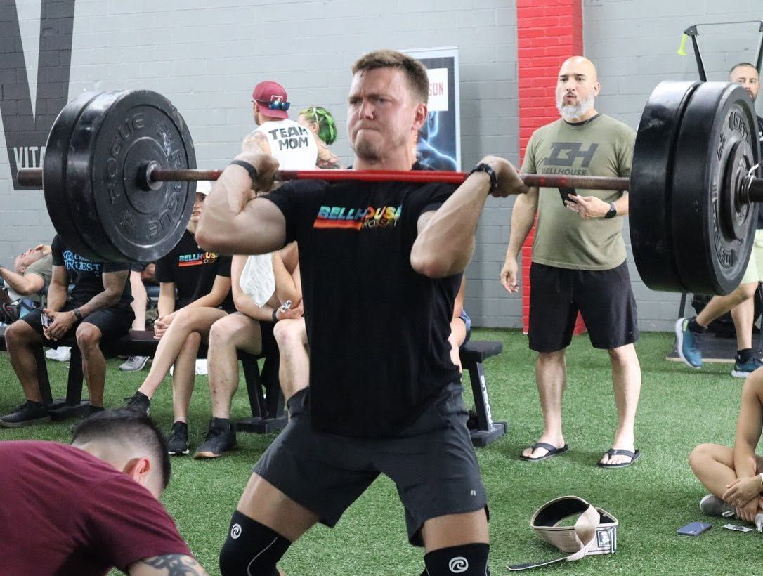 Weightlifter performing a clean and jerk with a barbell in an indoor gym, spectators watching nearby