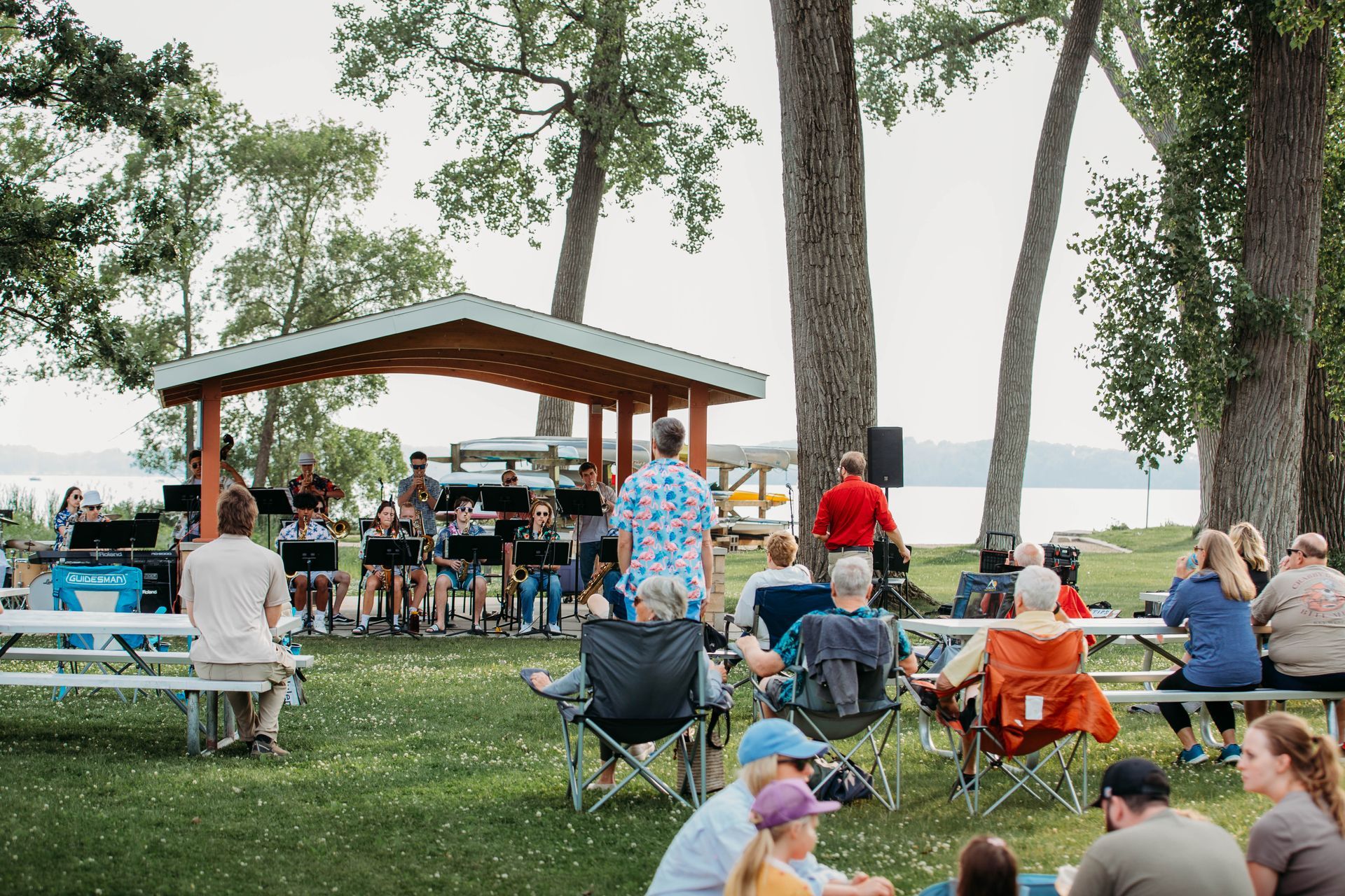 A group of people are sitting at picnic tables in front of a band.