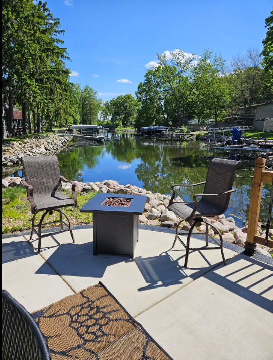 Patio with two chairs, fire pit, and view of a calm river on a sunny day.