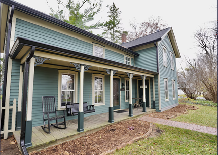 A large blue house with a porch and rocking chairs on it.