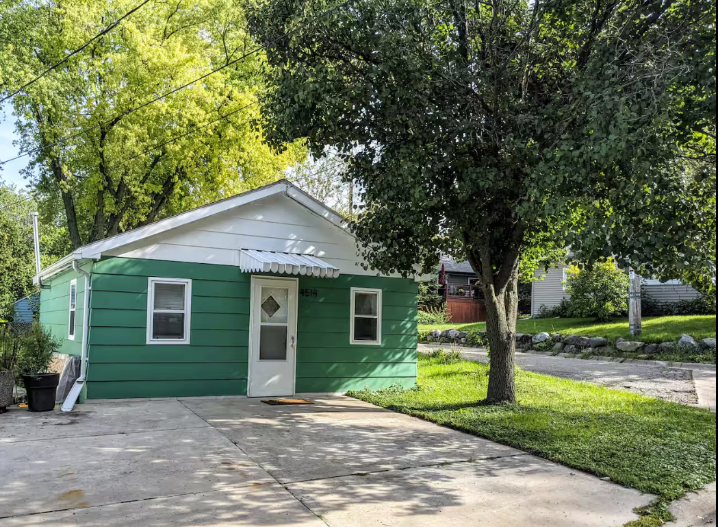 A small green house with a white roof and a tree in front of it.