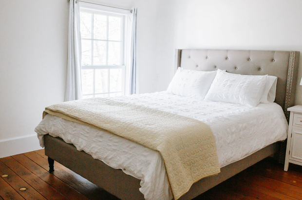 A bed with white sheets and pillows is in a bedroom next to a window.