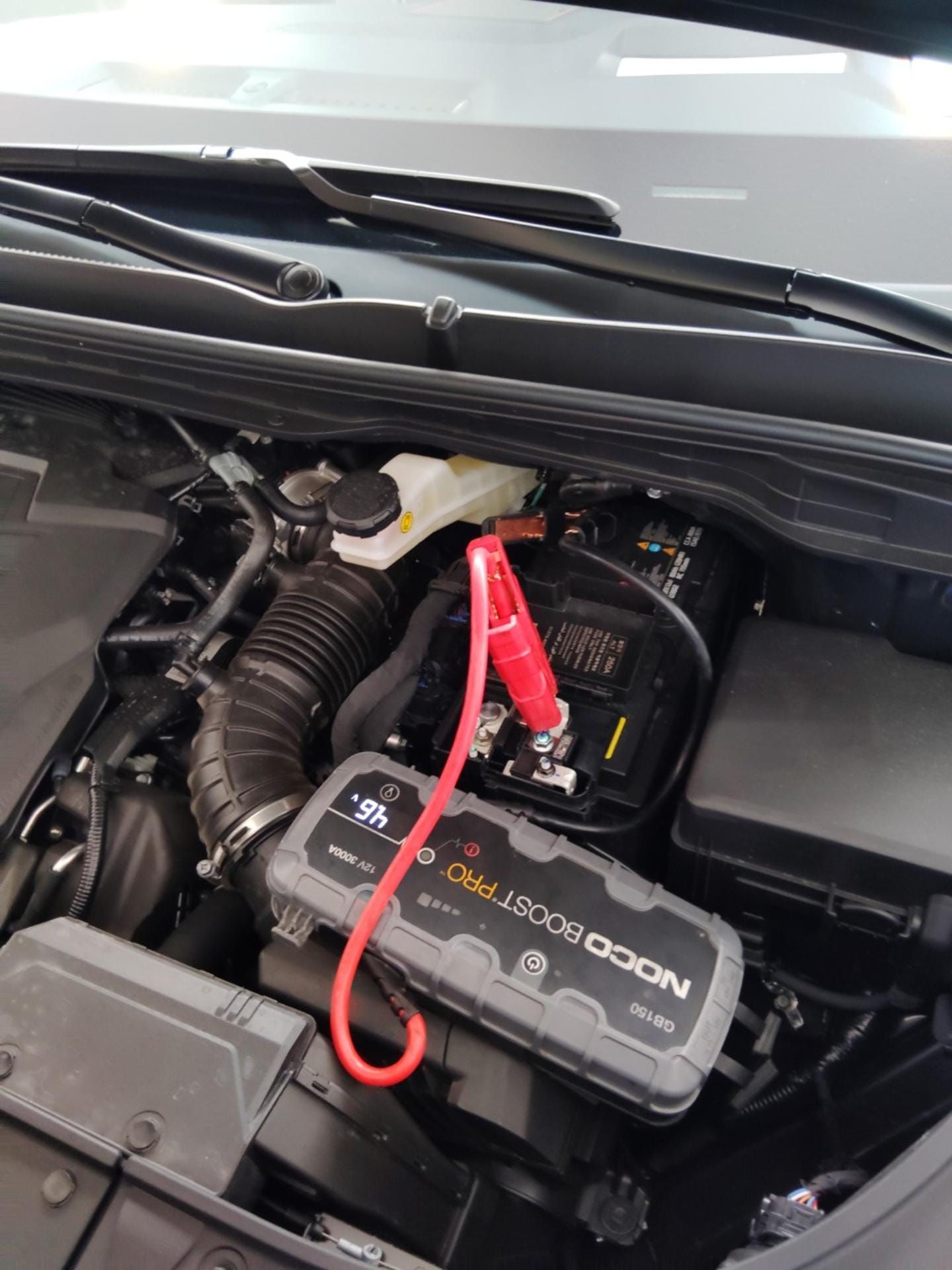 A car engine bay with a NOCO Boost jump starter connected to the battery to jump start the car.