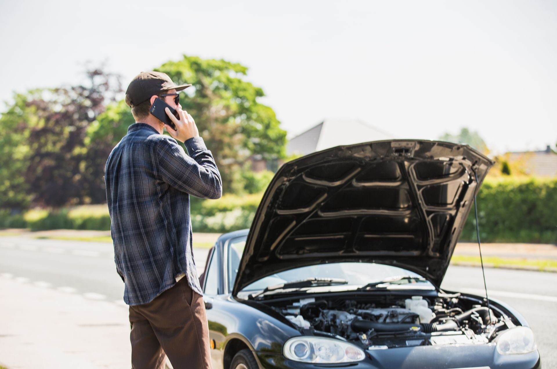 Man on phone next to car with open hood on roadside.