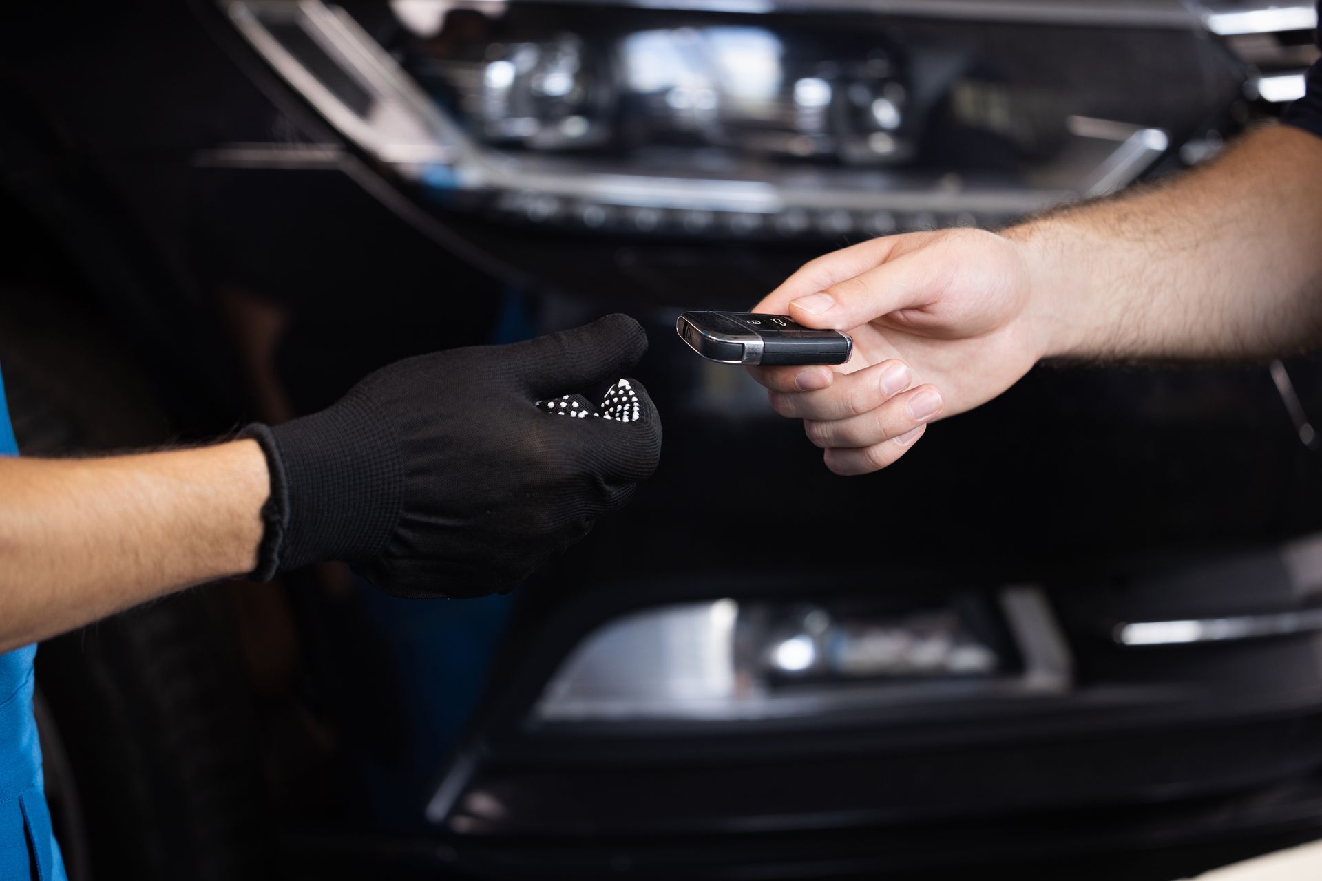 Person in black glove receiving car keys from another person near car.