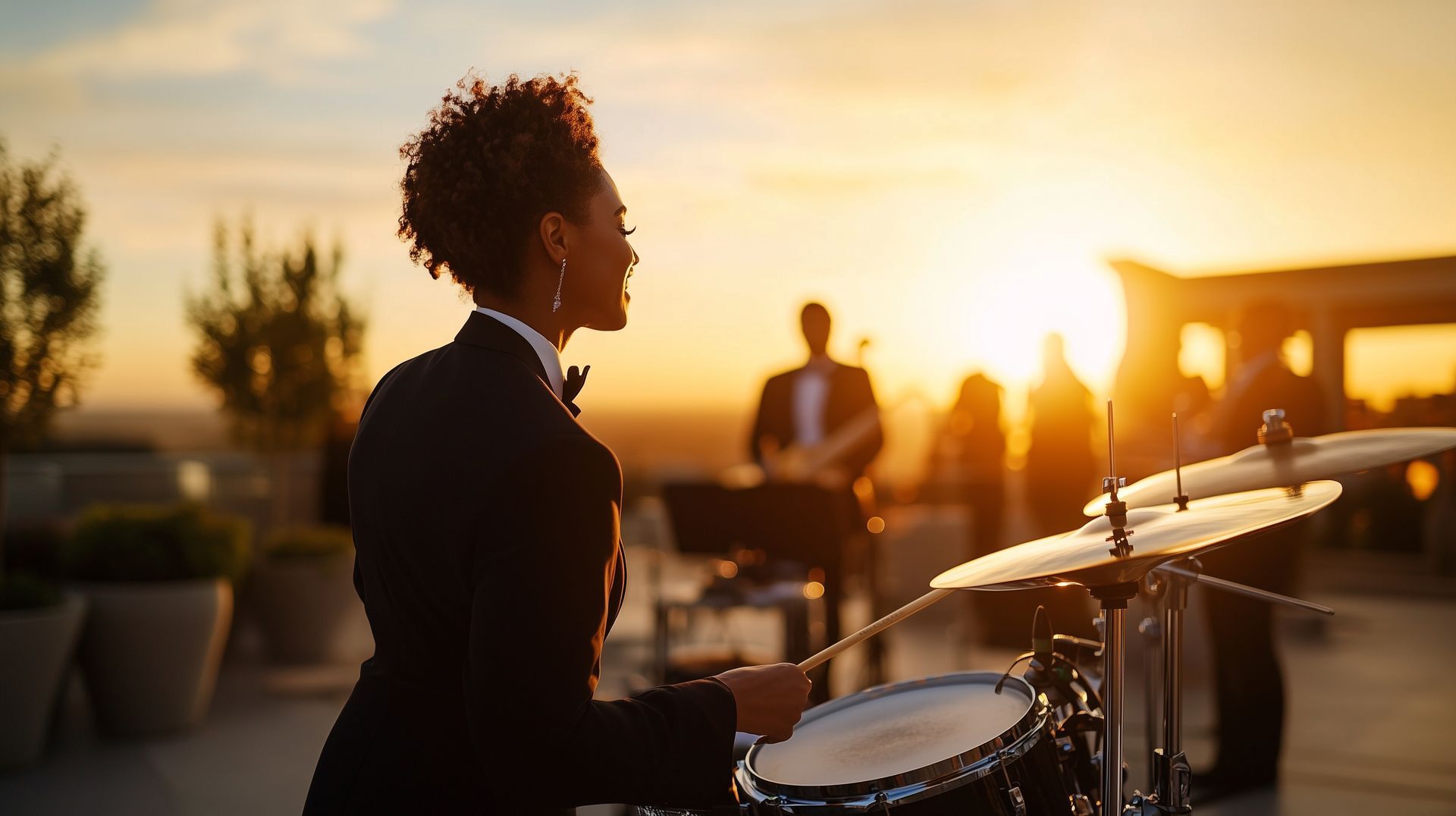 A woman in a tuxedo is playing drums at sunset.