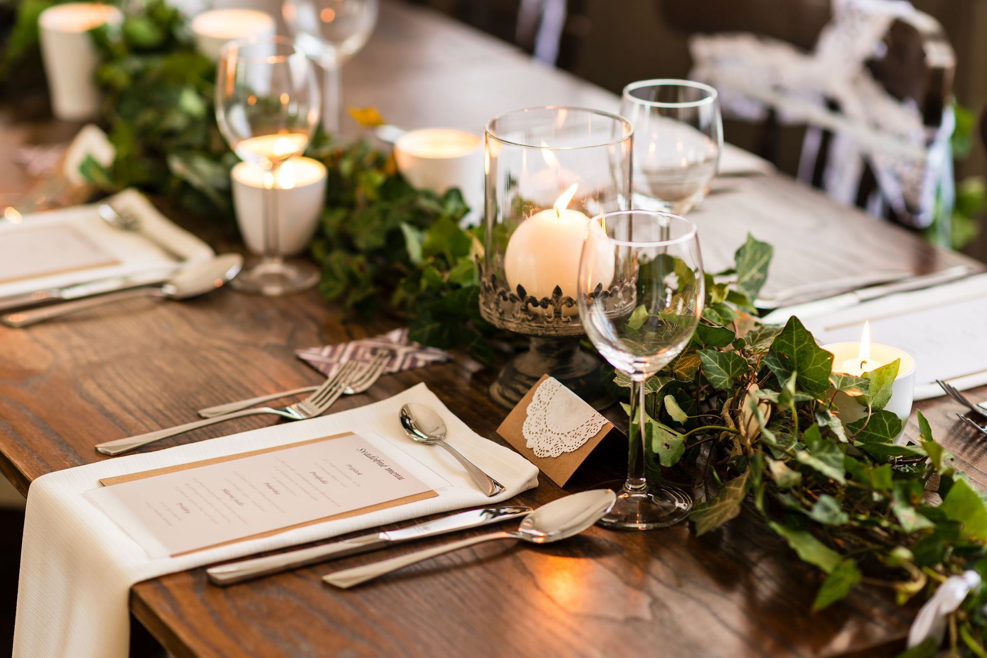 A long wooden table with plates , silverware , candles and a garland.