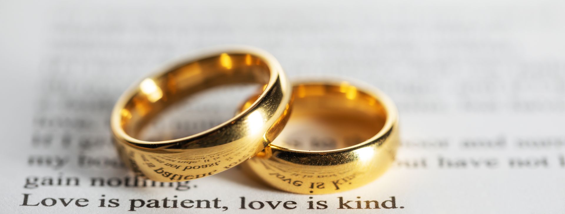 Two gold wedding rings on top of a book that says love is patient love is kind