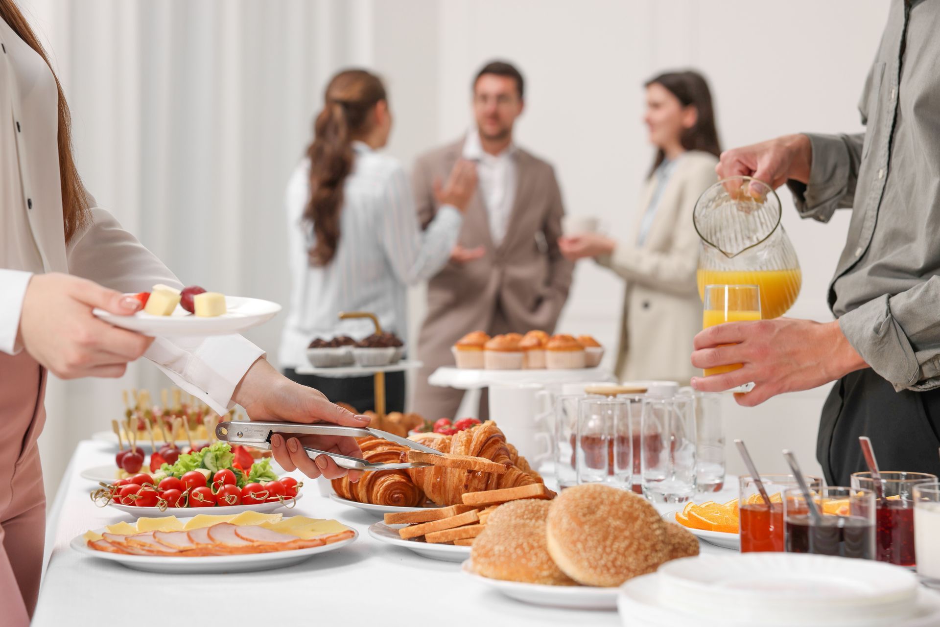 A group of people are standing around a table with food and drinks.