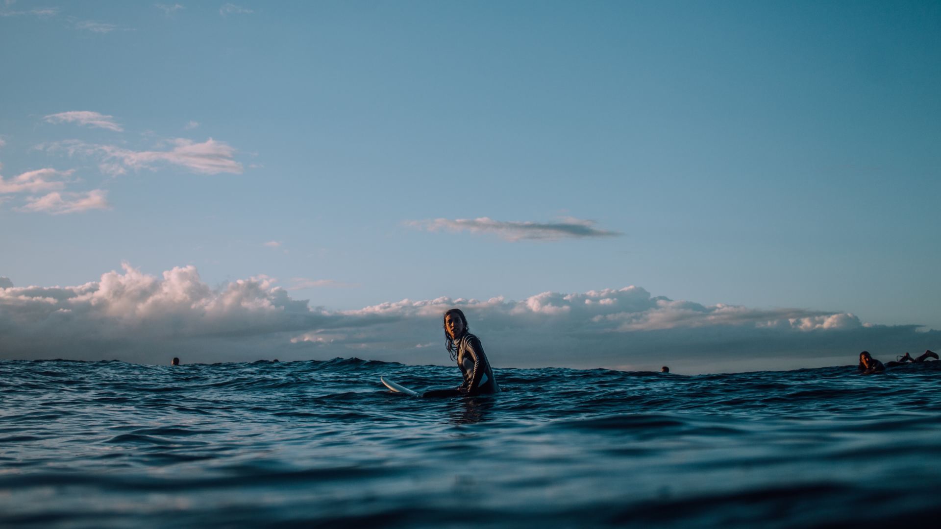 Imagem de um surfista na Nova Zelândia, sentado em sua prancha esperando para pegar uma onda em Piha, Nova Zelândia
