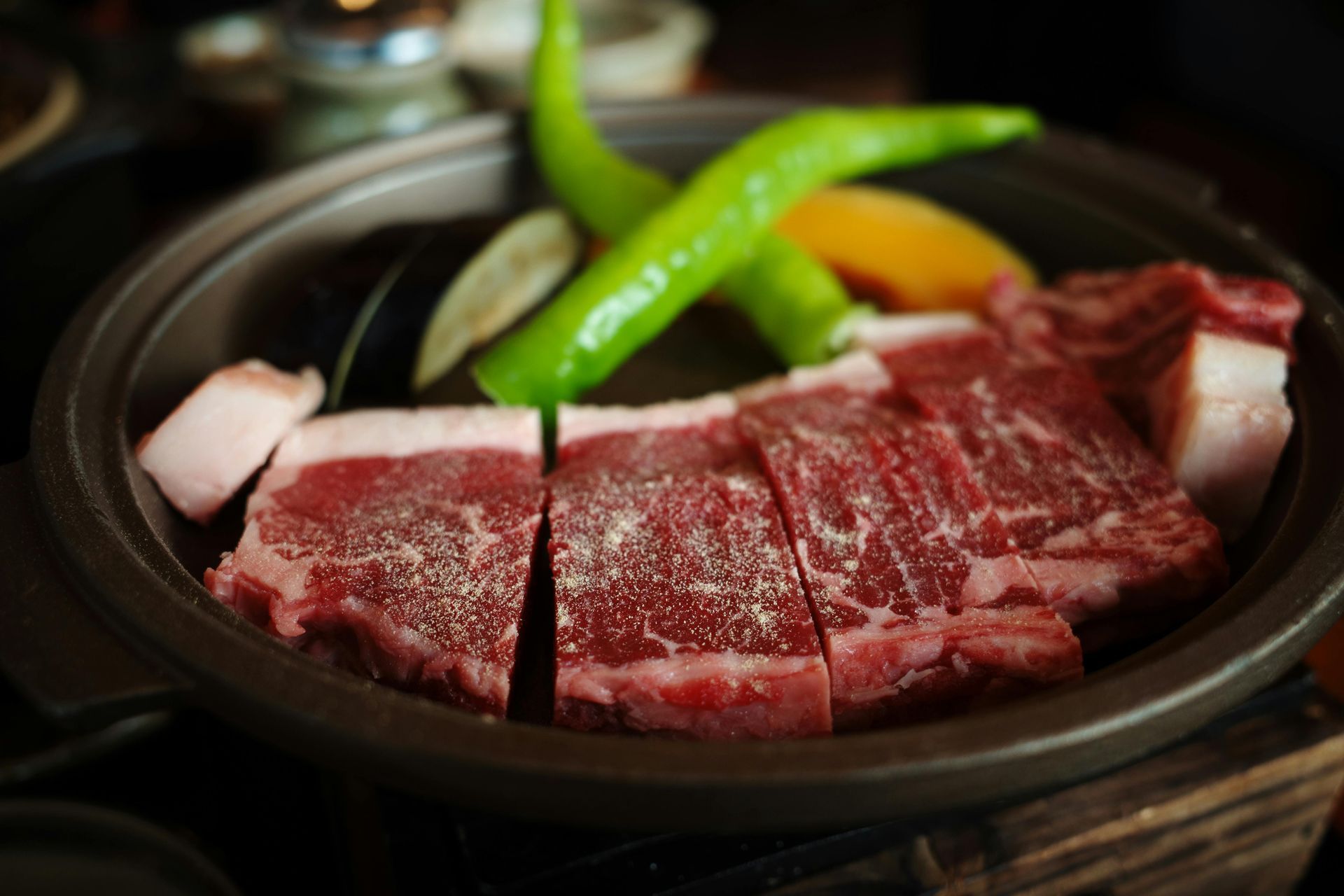 A thick, raw ribeye steak with heavy marbling rests on a wooden cutting board against a gray background.