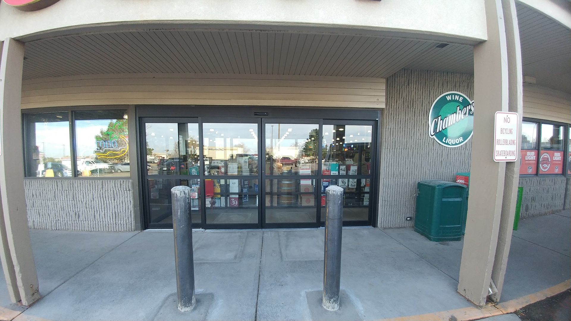 Exterior of a store with automatic sliding glass doors, concrete columns, and a trash can.