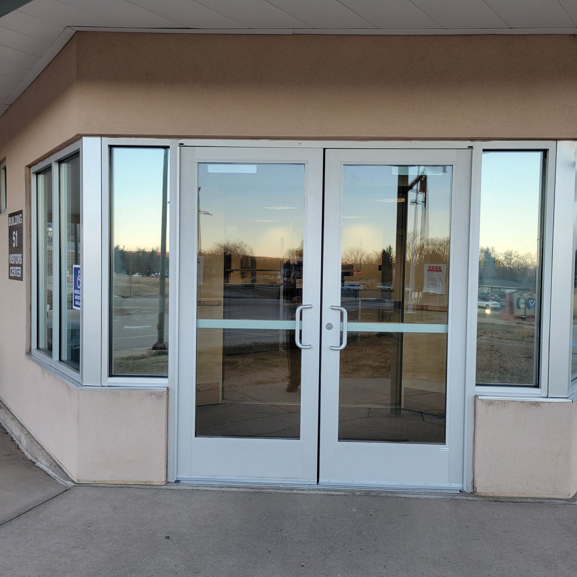 Double glass doors with side windows, reflecting outdoors. Cream-colored building exterior.