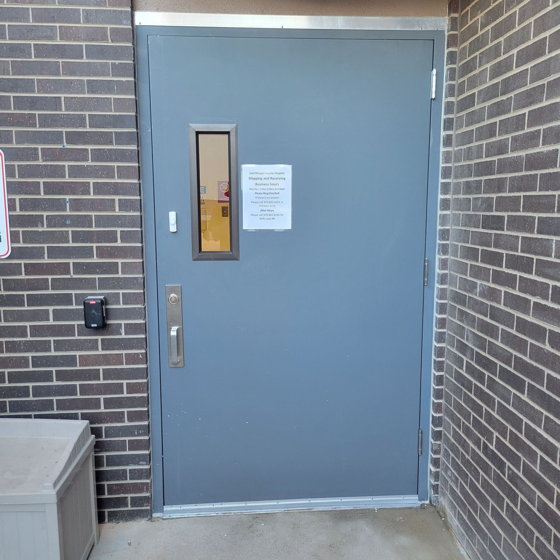Gray door in brick wall with small window and door handle. Access control pad on left.