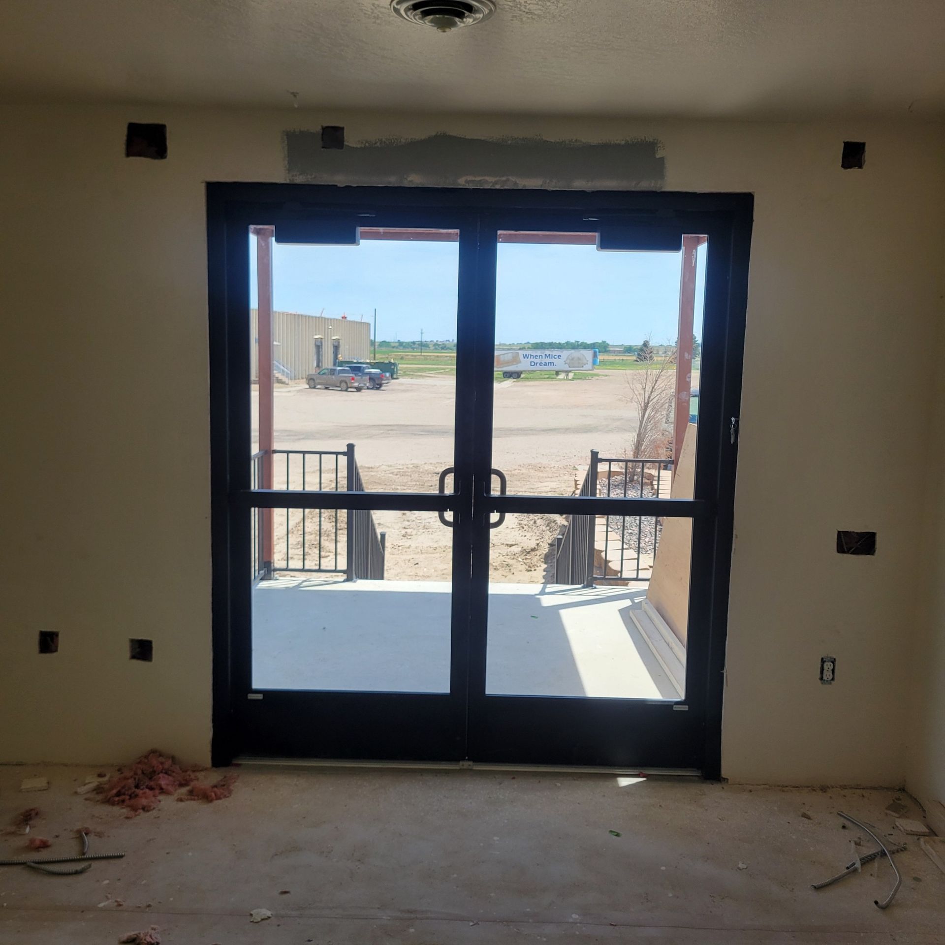 Double glass doors lead outside from an unfinished interior; a small set of steps leads to a gravel area.