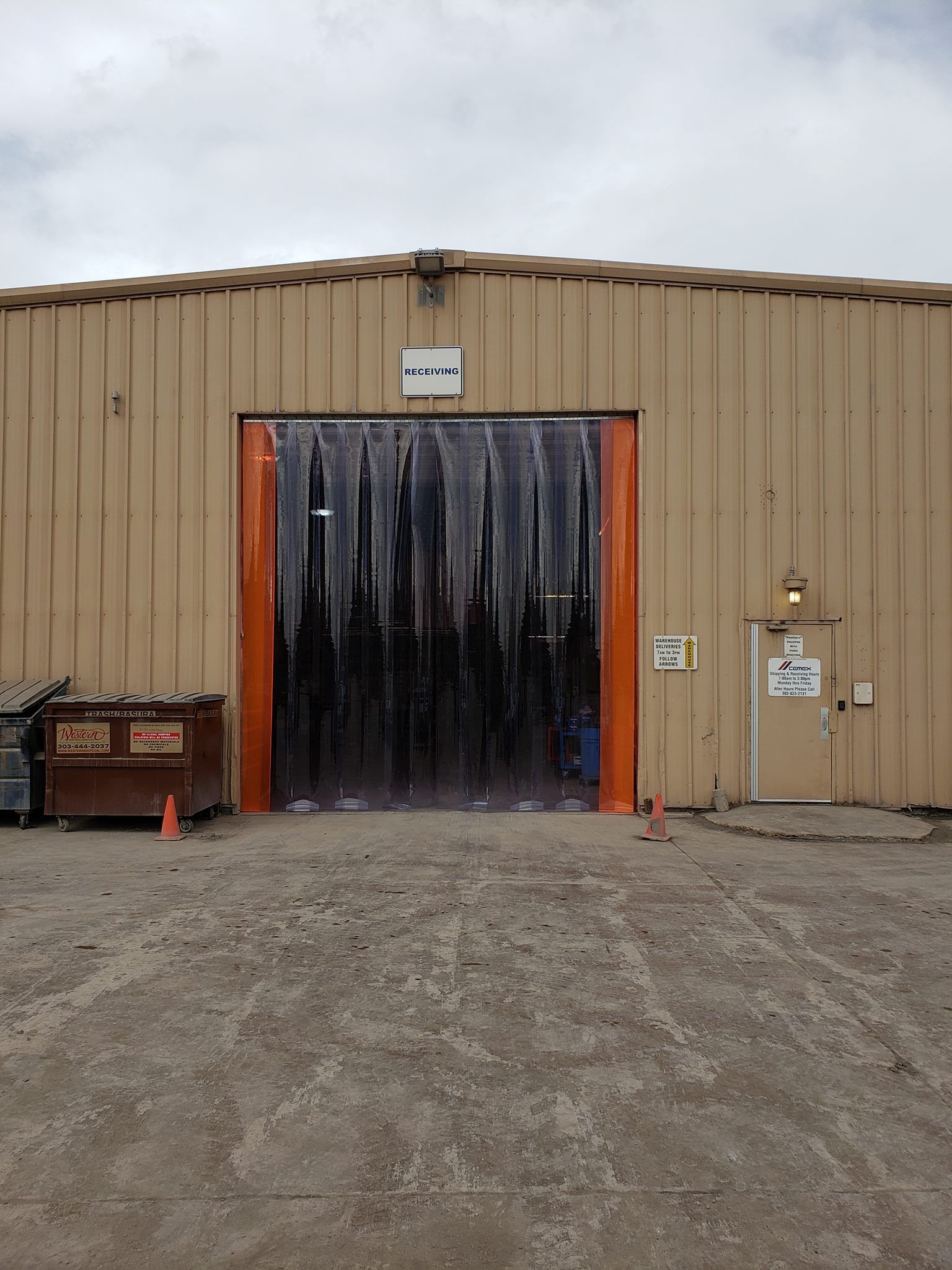 Warehouse entrance with plastic strip door, tan building, overcast sky.