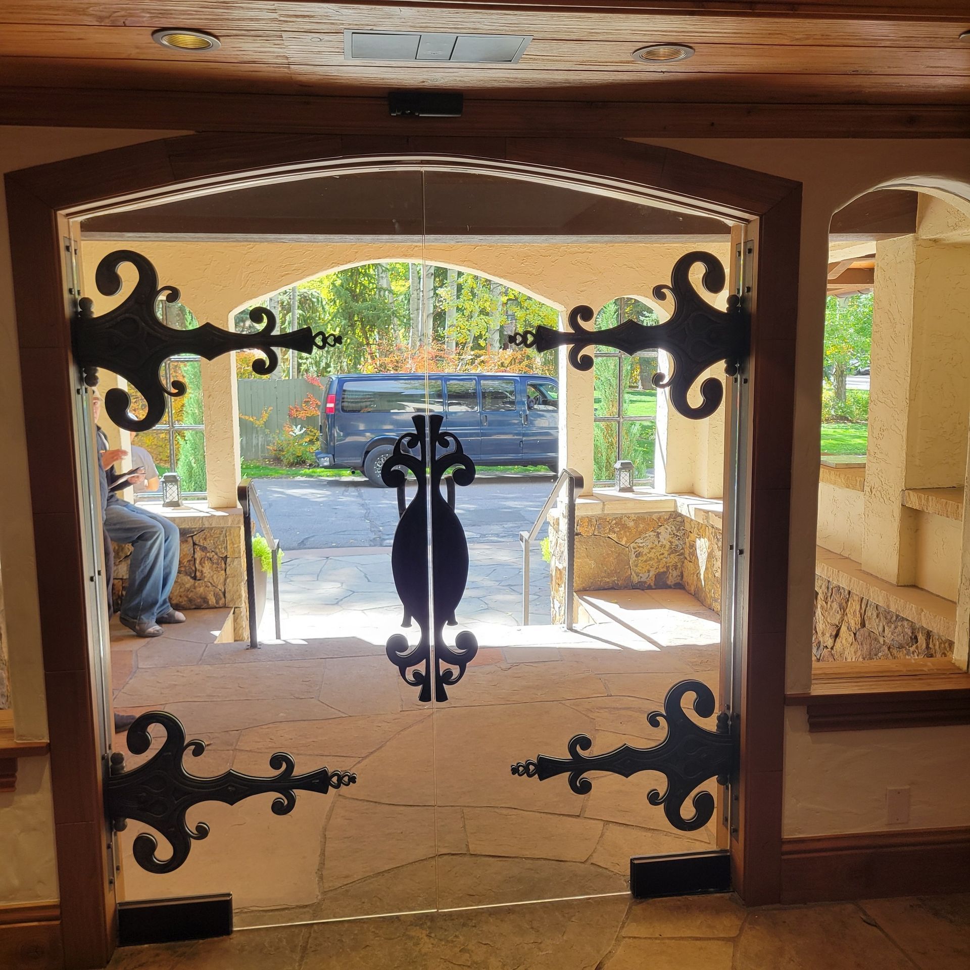 Ornate glass doors with ironwork, leading to an outdoor area with a person seated.