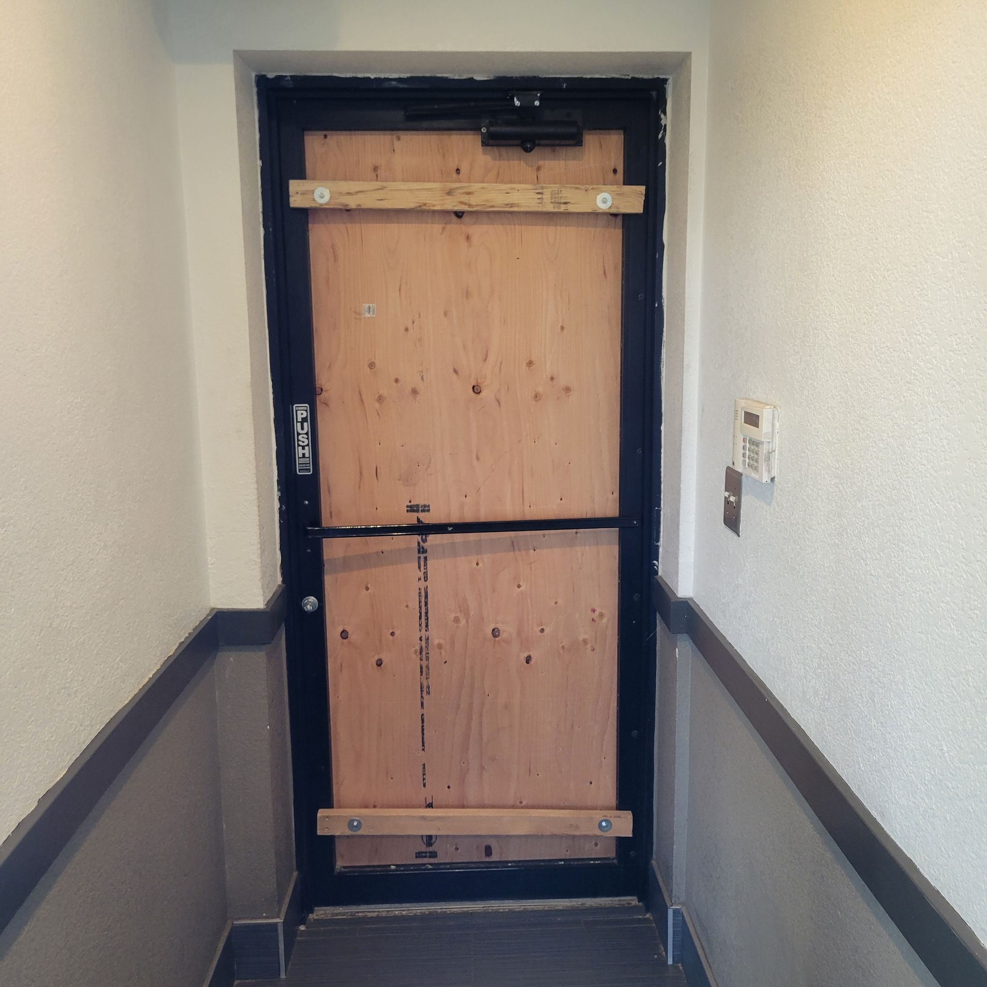 Boarded-up door in a narrow hallway. Light wood planks cover the door and are secured by horizontal wood pieces.