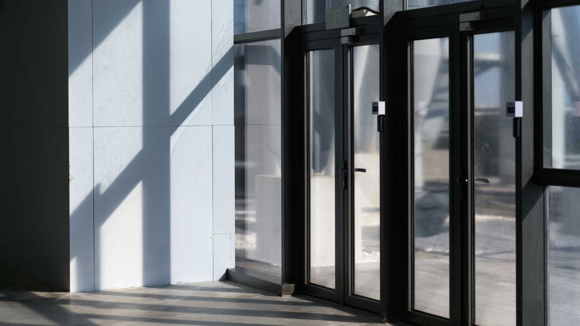 Sunlight on a white wall and glass doors, casting shadows.