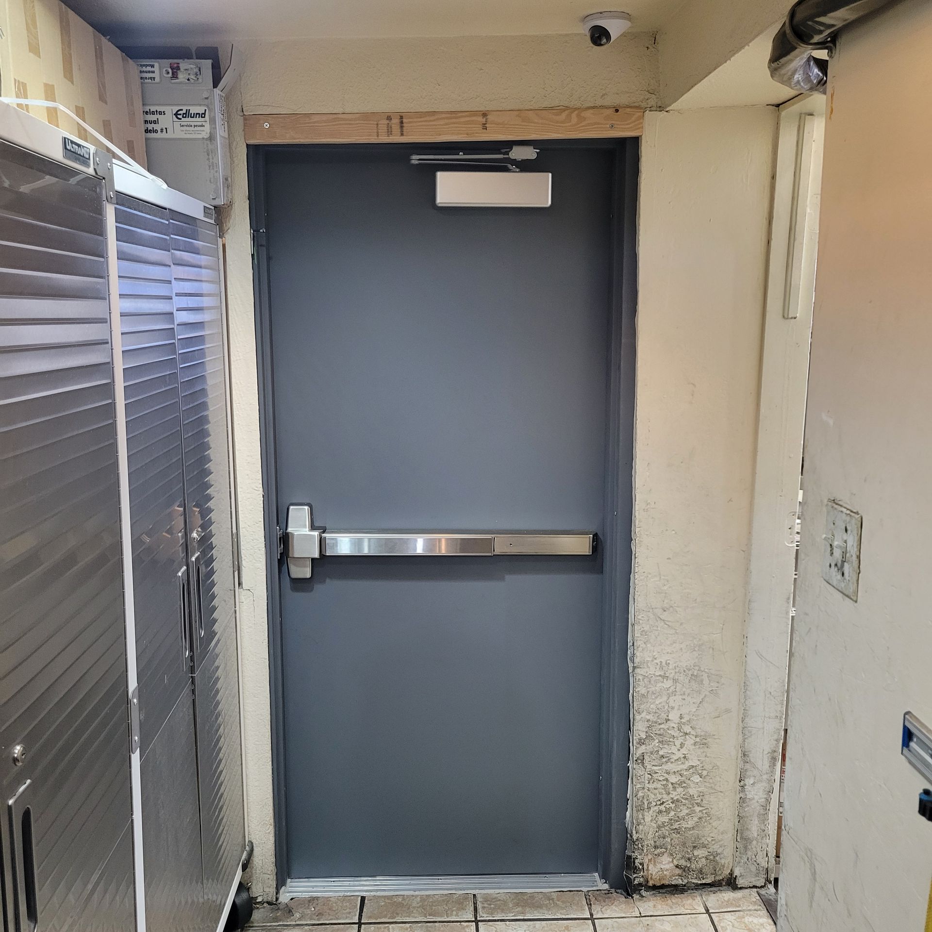 Gray door with a panic bar, in a commercial hallway.
