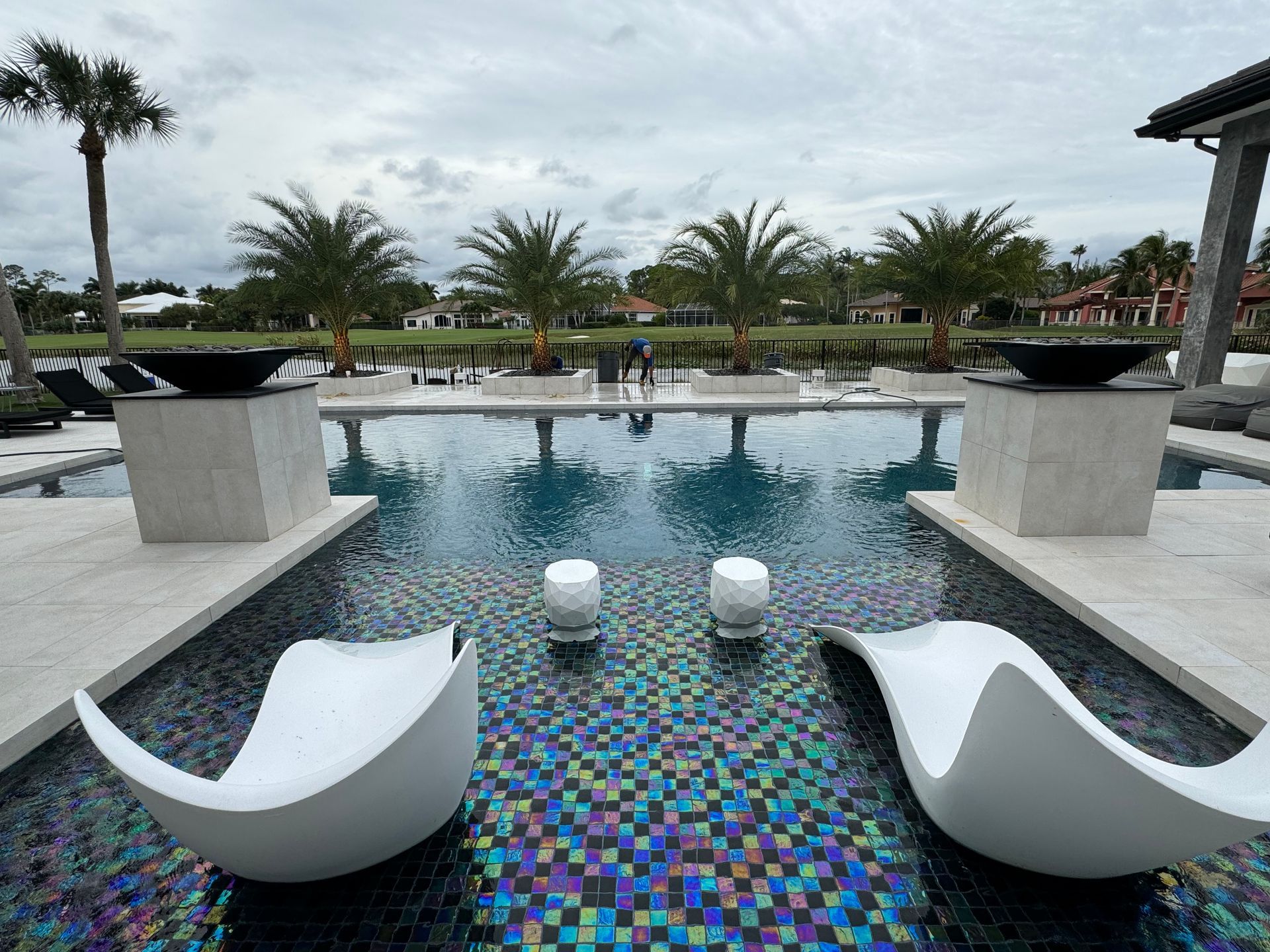 Two white chairs are sitting next to a large swimming pool.