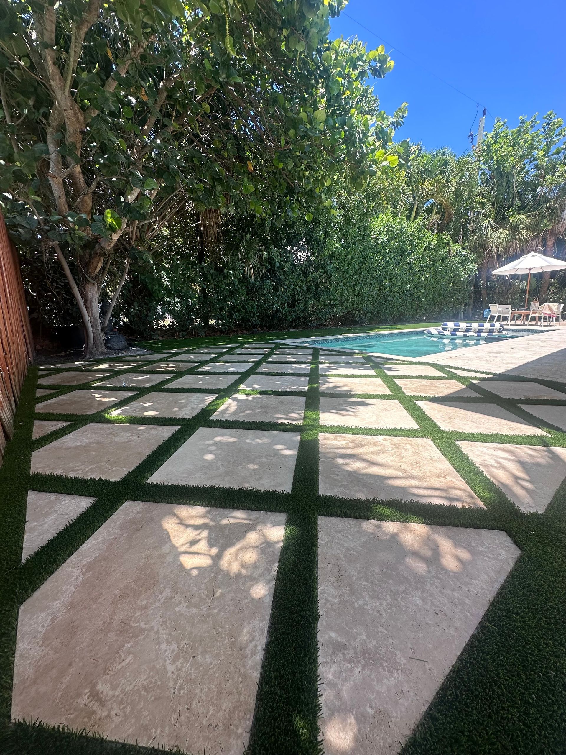 A patio with a swimming pool in the background and trees in the background.