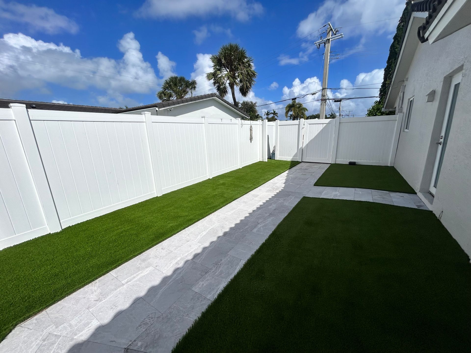 A white fence surrounds a lush green lawn in a backyard.