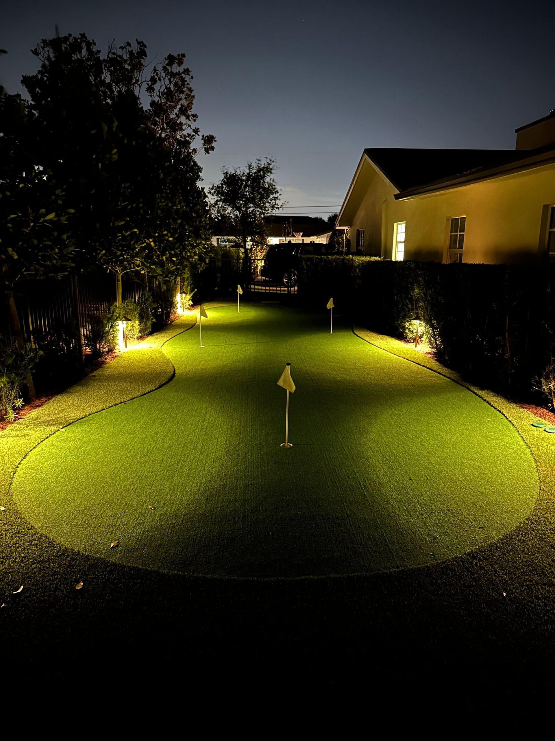 A golf course is lit up at night with a house in the background.