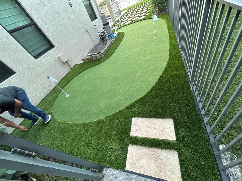 A man is playing golf on a putting green in a backyard.