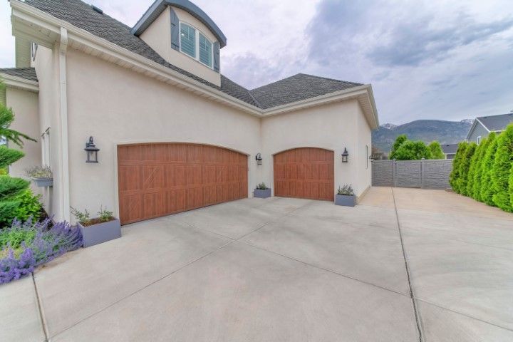 Light-colored house exterior featuring two wood-toned arched garage doors, concrete driveway, and mountain backdrop.