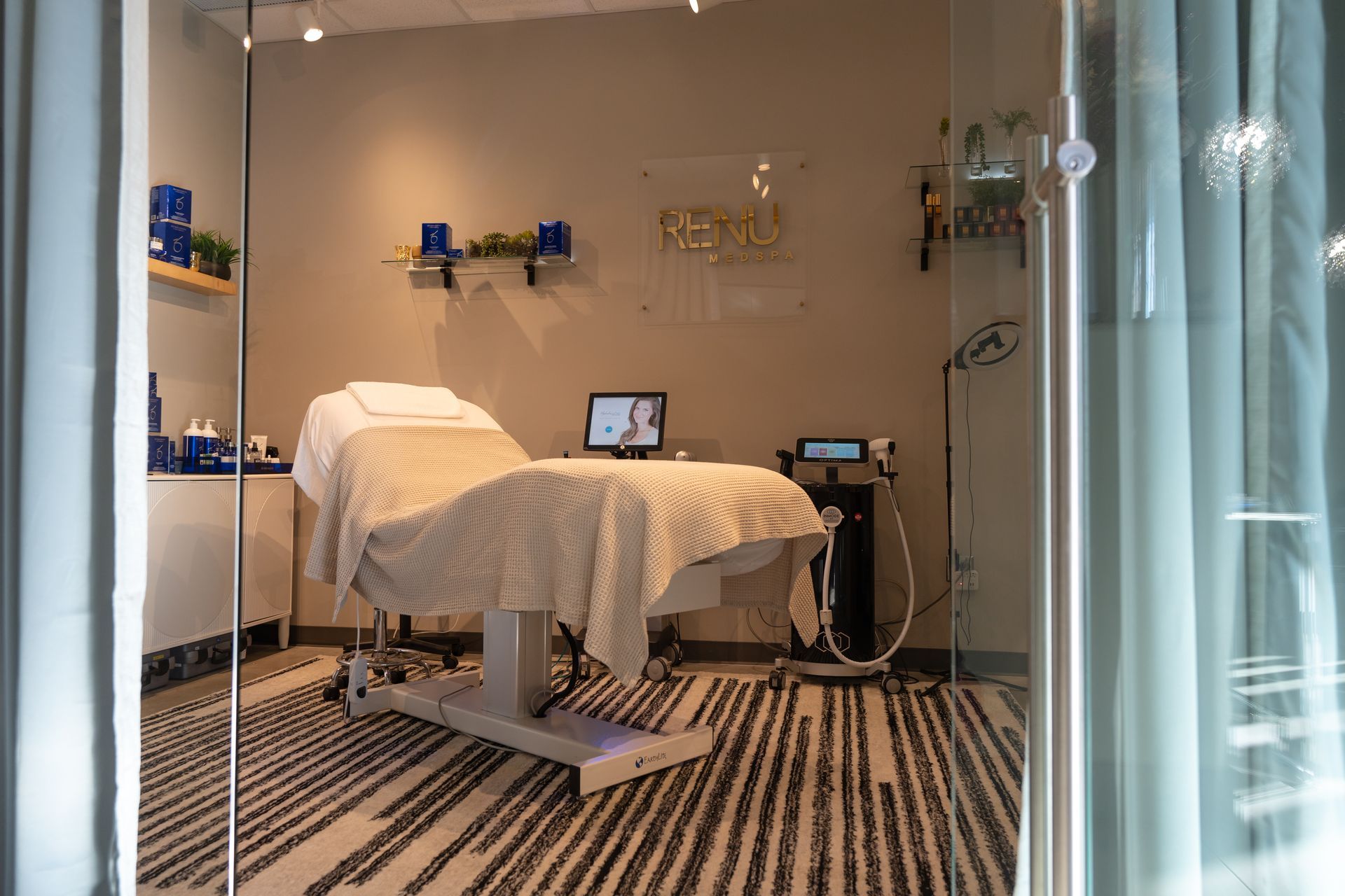 A medical spa treatment room with a bed, equipment, and shelves with skincare products.