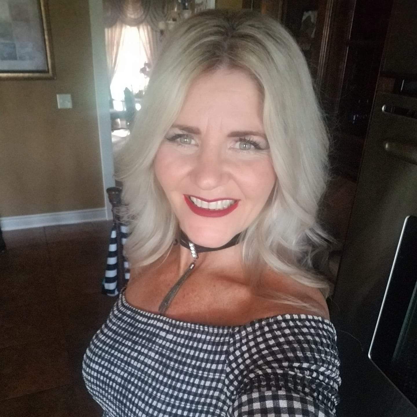 Woman with blonde hair smiling, wearing a black choker and striped off-the-shoulder top.