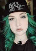 Person with green hair, black beanie, and black necklace, looking at the camera.