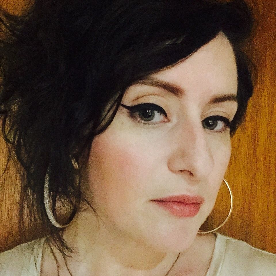 Woman with red hair and tattoos, resting chin on hand, wearing black clothing.