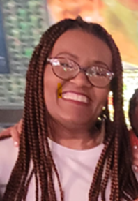 Woman with braided hair, glasses, and white top smiles. A blurred colorful background is behind her.