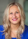 Blonde woman smiling, wearing a blue top, with a neutral background.