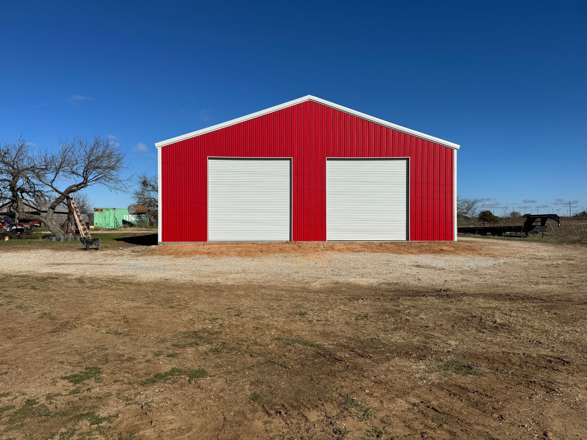A red barn with white doors is sitting in the middle of a dirt field.