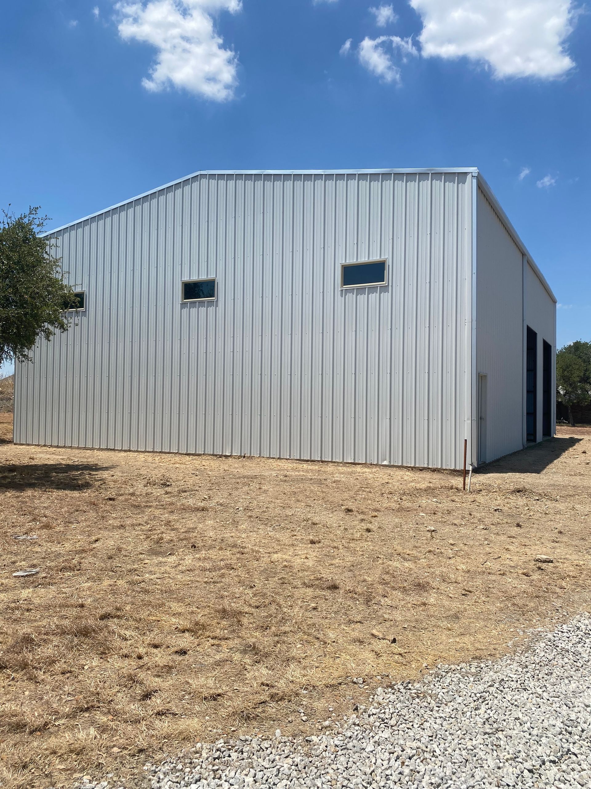 A large white building is sitting in the middle of a dry grass field.
