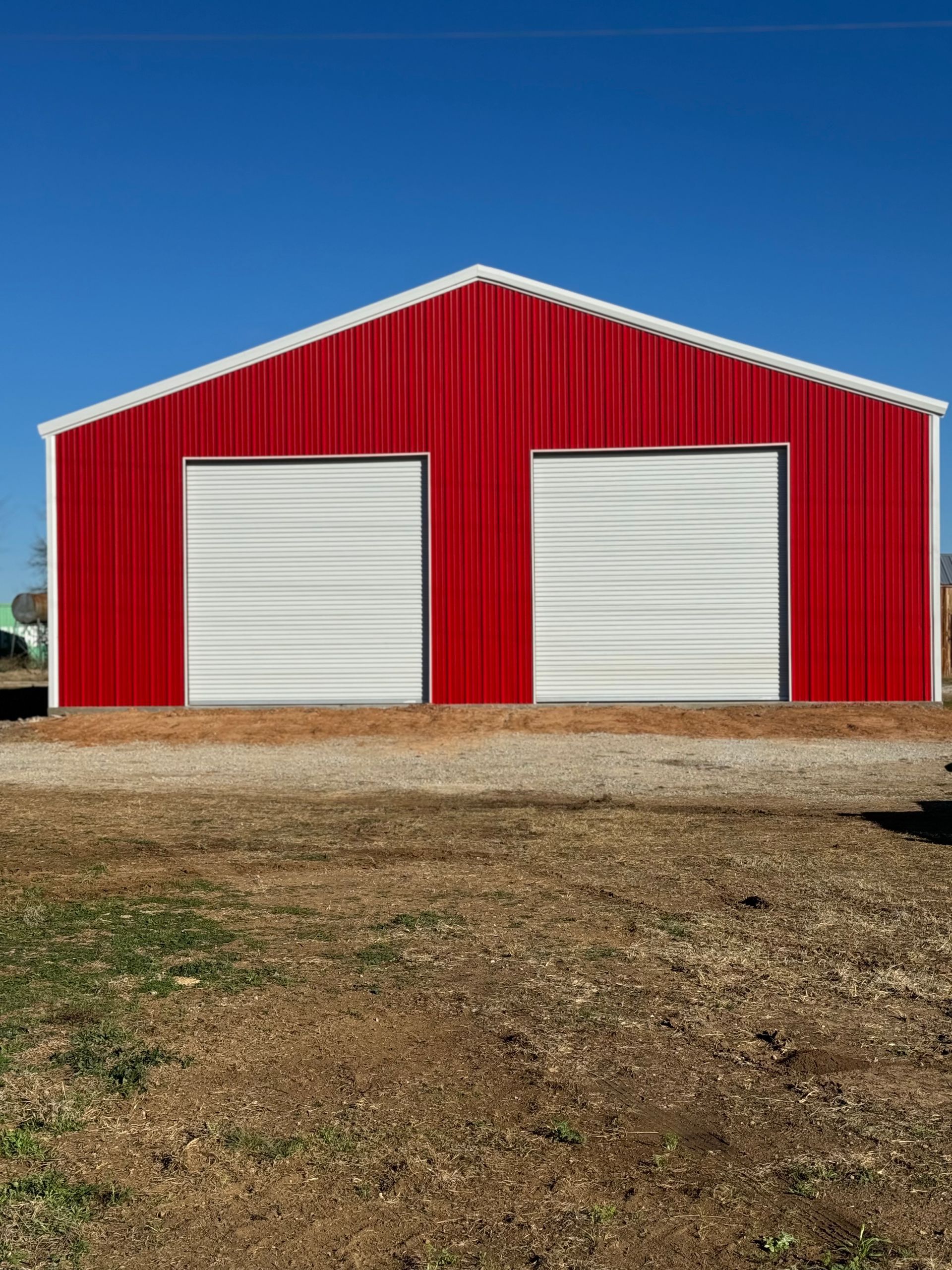 A red and white building with two garage doors is in a field.