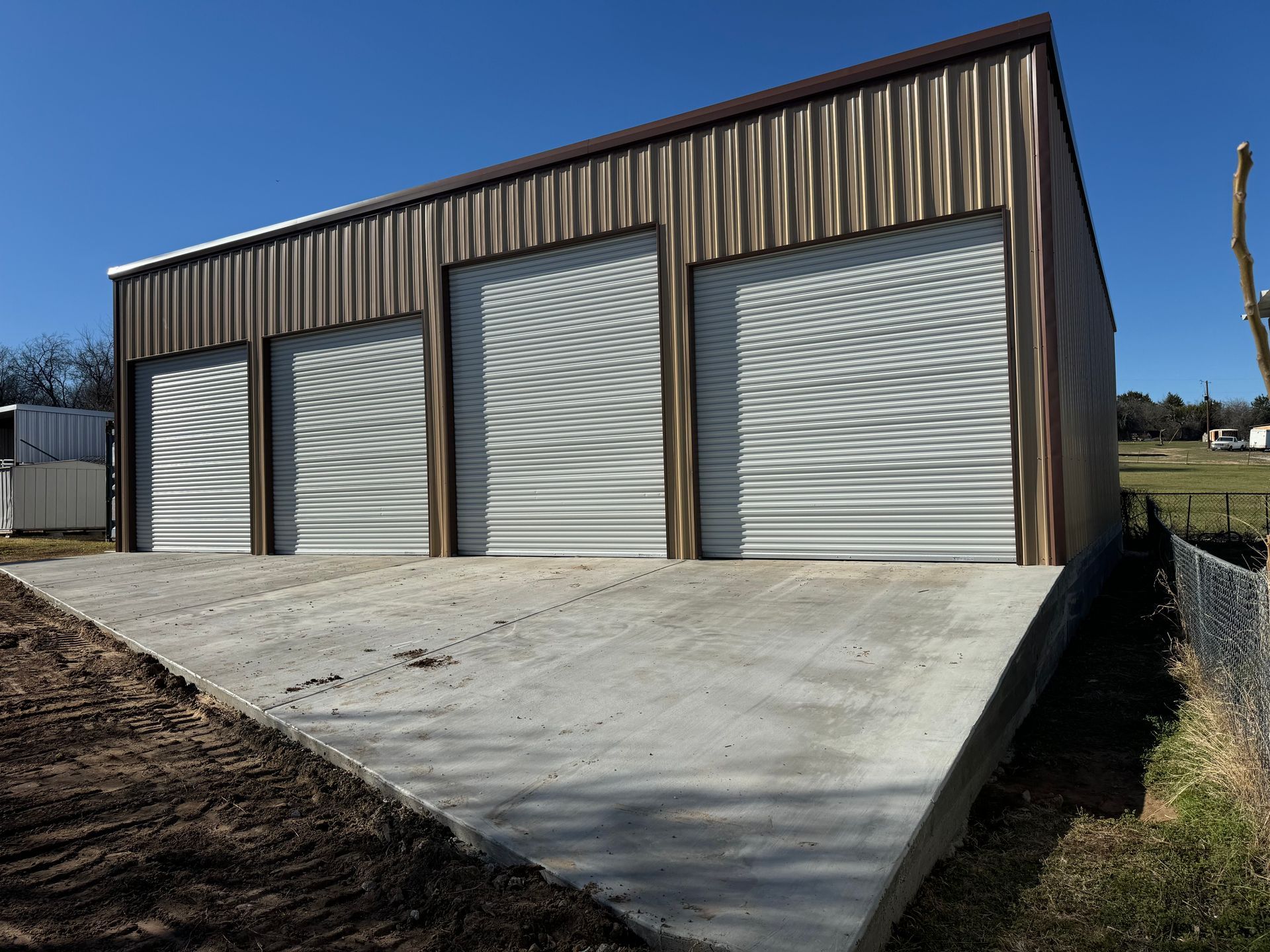 A large metal building with three garage doors and a concrete driveway.